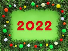 rosso provato nuovo anno numeri 2022 nel telaio fatto abete rami in giro su leggero verde sfondo. confine decorato colorato pom poms - bianca, giallo, arancia, rosso, verde. revisione di il anno. Natale 2022. foto