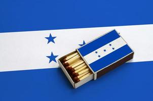 Honduras bandiera è mostrato nel un Aperto scatola di fiammiferi, quale è pieno con fiammiferi e bugie su un' grande bandiera foto
