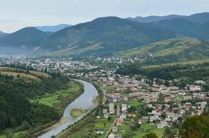 un' bellissimo Visualizza di il villaggio di mezhgorye, carpazi regione. un' lotto di Residenziale edifici circondato di alto foresta montagne e lungo fiume foto