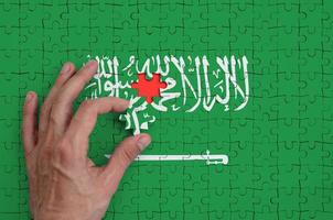 Arabia arabia bandiera è raffigurato su un' puzzle, quale il dell'uomo mano completa per piegare foto