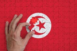 tunisia bandiera è raffigurato su un' puzzle, quale il dell'uomo mano completa per piegare foto