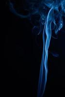 un' verticale tiro di blu tabacco Fumo su un' nero sfondo foto