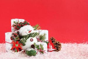 Natale ancora vita con regalo scatole avvolto di bianco-grigio carta con rosso bianco nastri su un' rosso sfondo, decorato di abete rami, pino cono, rosso di legno decorazioni e artificiale neve. foto