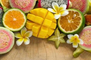 luminosa colorato tropicale frutta - Mango, mandarino, guaiava, Drago frutta, stella frutta, sapodilla con fiori di plumeria su il di legno sfondo. foto