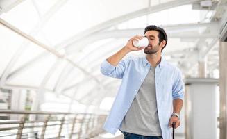 il uomo potabile un' tazza di caffè e traino il bagaglio mentre lui è in attesa il suo amico a il aeroporto. foto