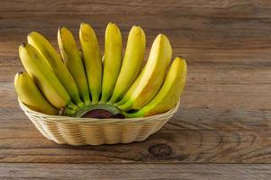 strappare mazzo di banane nel di vimini cestino su di legno sfondo. salutare mangiare concetto foto