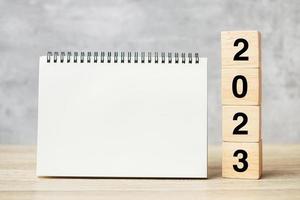 2023 felice anno nuovo con taccuino in bianco e numero di legno. conto alla rovescia, risoluzione, obiettivi, piano, azione e concetto di missione foto