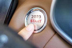 premere il dito sul pulsante di accensione dell'auto con il testo di inizio 2023 all'interno dell'automobile. nuovo anno nuovo te, previsione, risoluzione, motivazione, cambiamento, obiettivo, visione, innovazione e concetto di pianificazione foto