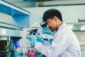 asiatico uomo scienziato utilizzando un' microscopio nel un' chimico laboratorio foto