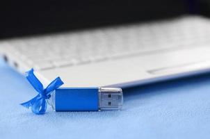 brillante blu USB veloce memoria carta con un' blu arco bugie su un' coperta di morbido e peloso leggero blu vello tessuto accanto per un' bianca il computer portatile. classico femmina regalo design per un' memoria carta foto