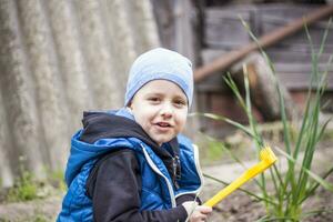 un' bambino è piantare un' giardino. un' del bambino rastrello nel il suo mani. un' poco giardiniere ragazzo è piantare impianti nel un' fiore letto. giardinaggio utensili nel il mani di un' bambino. foto