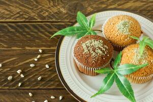 salutare e gustoso vegano e glutine gratuito muffin sormontato con canapa semi su un' bianca piatto su di legno tavolo. marijuana Cupcake muffin con canapa le foglie foto