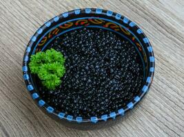 caviale nero in una ciotola su fondo di legno foto