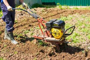 aratura il terra nel il giardino con un' Coltivatore. agricolo opera su aratura il campo per semina semi. un' uomo aratri il terra utilizzando il motore Coltivatore. foto