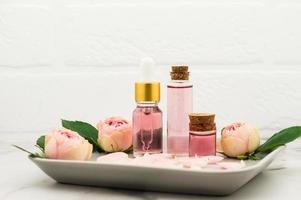 cosmetico rosa olio o essenziale olio, rosa acqua su un' ceramica vassoio contro un' bianca mattone parete. idratante, aromaterapia. foto