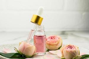 un Aperto bottiglia di rosa olio e un' pipetta pieno con cosmetici per ringiovanimento e facciale pelle cura su un' ceramica piatto. foto