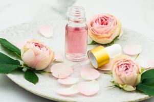 un Aperto bottiglia di rosa olio e un' pipetta pieno con cosmetici per ringiovanimento e facciale pelle cura su un' ceramica piatto. foto