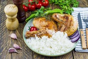 un' piatto di grigliato fritte pollo e bollito Riso. pomodori, galletto verdi, aglio su un' di legno tavola. rustico di legno sfondo. foto