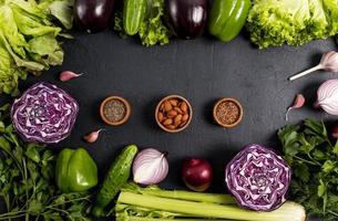 telaio di biologico verdure per cucinando salutare pasti. viola e verde verdure. noccioline, semi nel di legno ciotole. superiore Visualizza. nero sfondo.