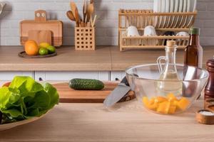 davanti Visualizza di il cucina tavolo con insalata ingredienti. il sfondo di un' moderno cucina con domestico utensili su il controsoffitto. foto