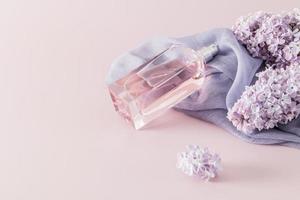 un' elegante bottiglia di Da donna profumo o eau de parfum bugie su un' donna di accessorio - un' sciarpa e lilla fiori. spazio per testo. rosa sfondo. foto