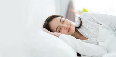 bellissimo asiatico donna posa su il letto con cuscini comodamente supportato. e sorridente felicemente foto