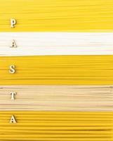 un' sfondo di asciutto lungo pasta, tagliatelle e spaghetti con un' parola di di legno lettera- pasta. superiore Visualizza. piatto posizione. foto