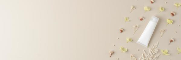 bianca tubo di cosmetico crema con fiori su pastello beige sfondo. piatto posizione, copia spazio foto
