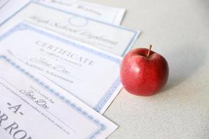 un' onore rotolo riconoscimento, certificato di realizzazione e alto scuola diploma bugie su tavolo con rosso Mela. formazione scolastica documenti foto