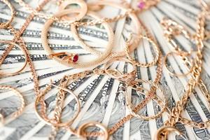 molti costoso d'oro jewerly anelli, orecchini e collane su grande quantità di noi dollaro fatture vicino su. banco dei pegni o jewerly negozio foto