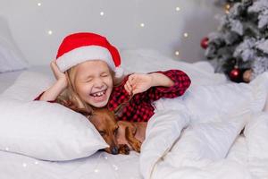 poco ragazza dorme nel letto con un' bassotto cane per Natale foto