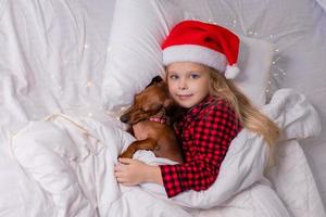 poco ragazza dorme nel letto con un' bassotto cane per Natale foto