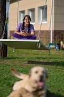 un' adolescente ragazza altalene su un' swing con un' Telefono nel sua mani, comunica nel sociale reti o impara in linea foto