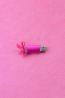 brillante rosa USB veloce memoria carta con un' rosa arco bugie su un' coperta di morbido e peloso leggero rosa vello tessuto. classico femmina regalo design per un' memoria carta foto