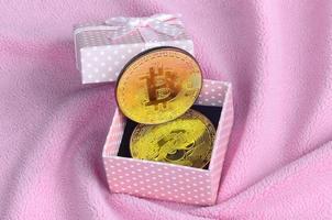 il d'oro bitcoin bugie nel un' piccolo rosa regalo scatola con un' piccolo arco su un' coperta fatto di morbido e soffice leggero rosa vello tessuto con un' grande numero di sollievo pieghe foto