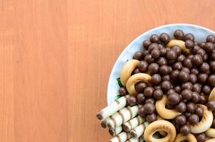 croccante tubuli, cioccolato fusione palle e bagel menzogna nel un' bianca piatto su un' di legno tavolo. mescolare di vario dolci foto