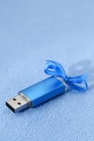 brillante blu USB veloce memoria carta con un' blu arco bugie su un' coperta di morbido e peloso leggero blu vello tessuto. classico femmina regalo design per un' memoria carta foto