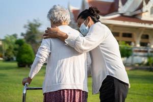 badante Aiuto e cura asiatico anziano o anziano vecchio signora donna uso camminatore con forte Salute mentre a piedi a parco nel contento fresco vacanza. foto