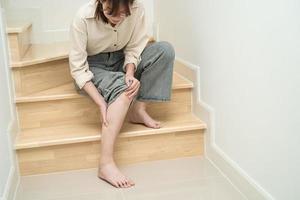 asiatico signora donna toccare e sentire dolore sua ginocchio su il le scale a casa, salutare medico concetto. foto