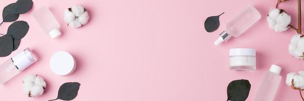 cosmetico pelle cura prodotti con fiori e eucalipto su rosa sfondo. piatto posizione, copia spazio foto