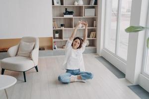 femmina praticante yoga su pavimento nel vivente camera, allungamento braccia su. salutare stile di vita, benessere foto