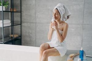 bella donna godere aroma di naturale cura della pelle cosmetici per corpo cura seduta nel moderno bagno foto