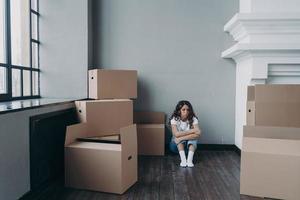 triste donna seduta su il pavimento tra scatola di cartone scatole con cose per in movimento. divorzio, sfratto concetto foto