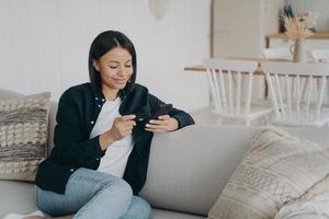 sorridente femmina Tenere banca credito carta, Telefono fa riuscito senza soldi pagamento su divano a casa foto