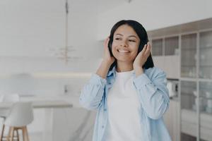 sorridente donna ascoltando per musica nel senza fili cuffia, godendo musicale suono riposo a casa foto