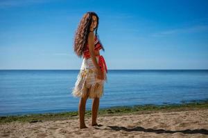 un' giovane donna sta su il spiaggia con sua indietro per il mare, su un' soleggiato giorno. il concetto di un' vacanza di il mare foto