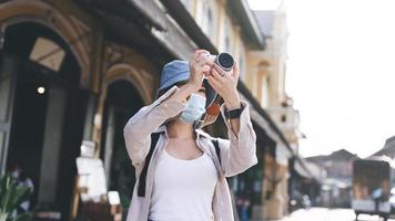 il viaggiatore dello zaino della giovane donna asiatica adulta indossa la maschera per il viso scatta una foto con la fotocamera.