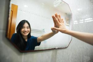 giovane adulto Sorridi asiatico donna pratica se stesso parlare conversazione con specchio nel il mattina foto