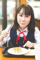 contento giovane asiatico donna nel giapponese uniforme alunno a bar godere gustoso volta. foto