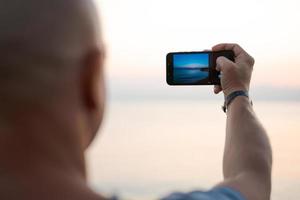 uomo assunzione foto sorprendente tramonto utilizzando smartphone telecamera, turista mano Tenere